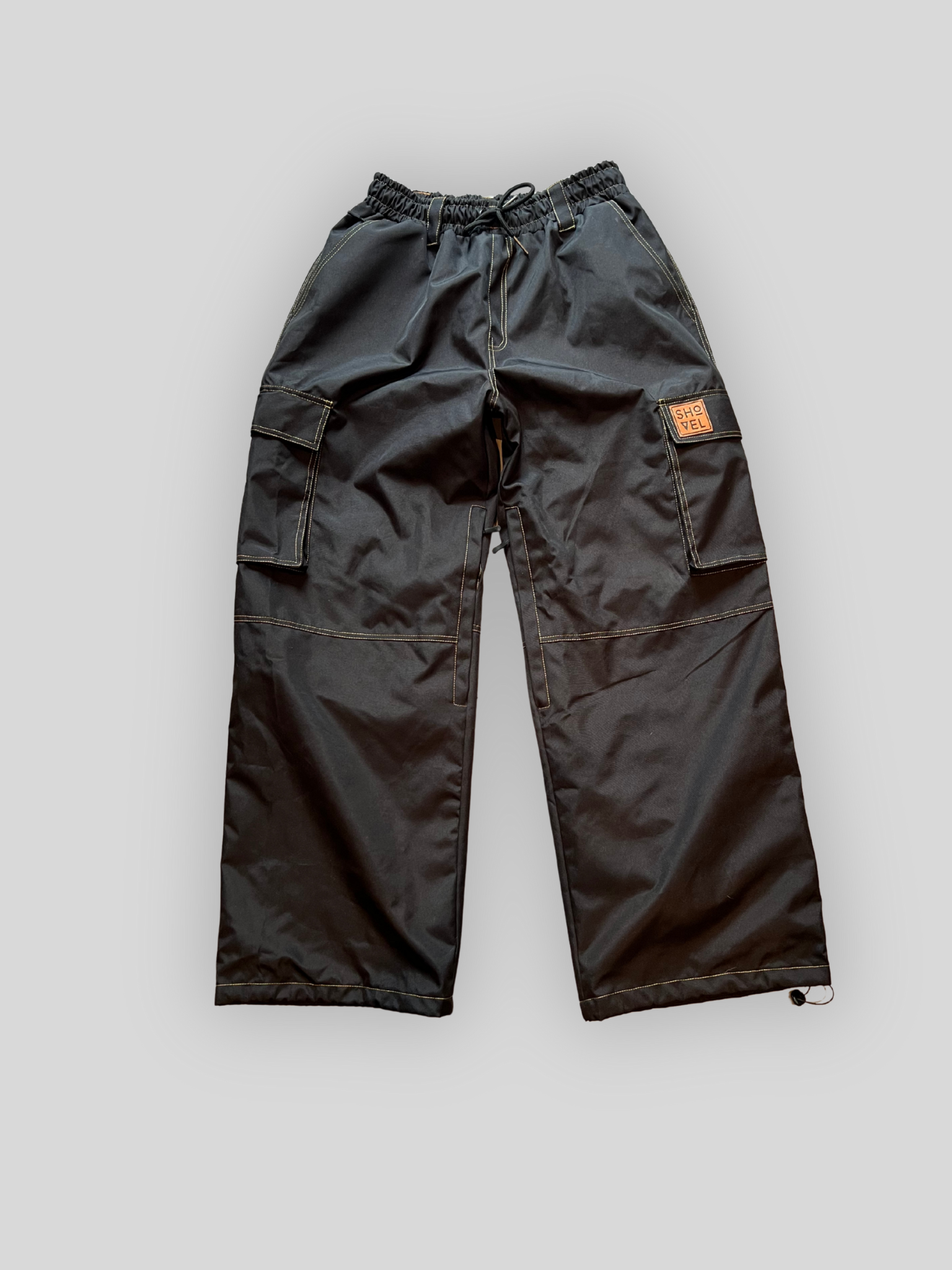 Black Jean style ski and snowboard cargo pants with a brand logo on a light gray background, front view.